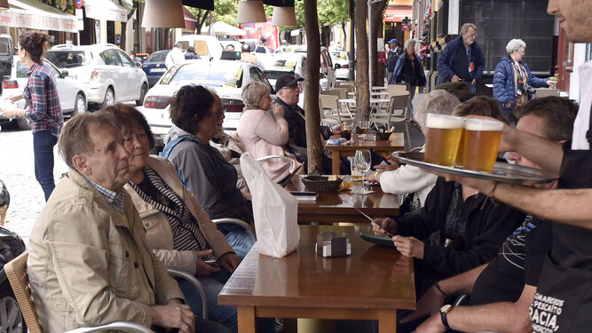 Un camarero lleva una bandeja con cervezas a los clientes de un velador.