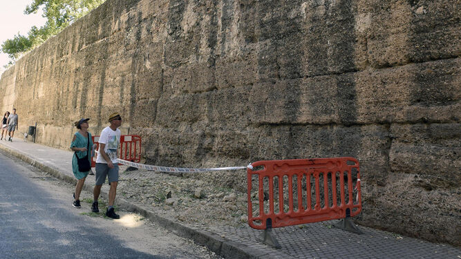 Dos viandantes observan la zona en la que ha caído una almena de la muralla de la Macarena.