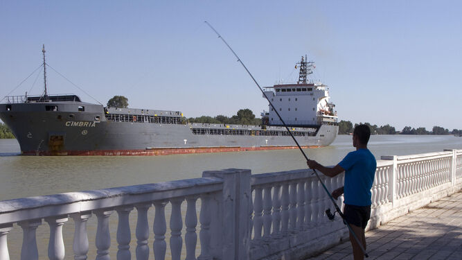 Un hombre pesca mientras un barco navega aguas arriba por el río Guadalquivir en Coria del Río.