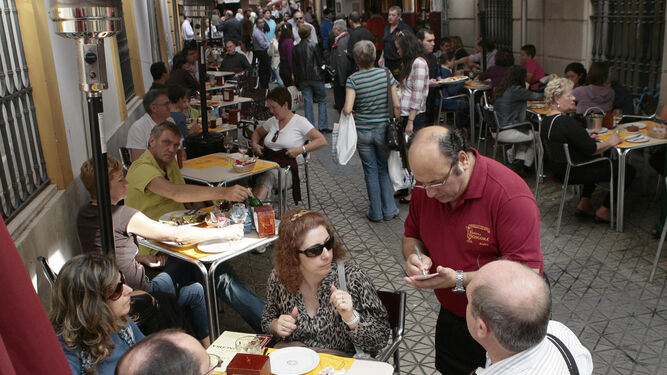 Un camarero atiende una mesa en una popular calle llena de bares en el centro de Sevilla.
