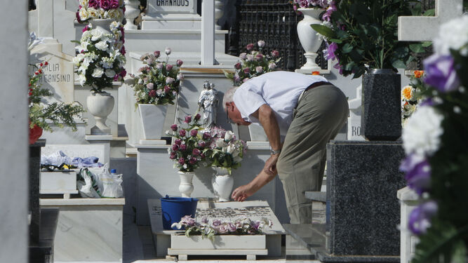 Un hombre deja flores sobre una lápida.