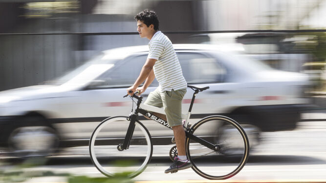 Un joven circulando en bicicleta junto a un automóvil.