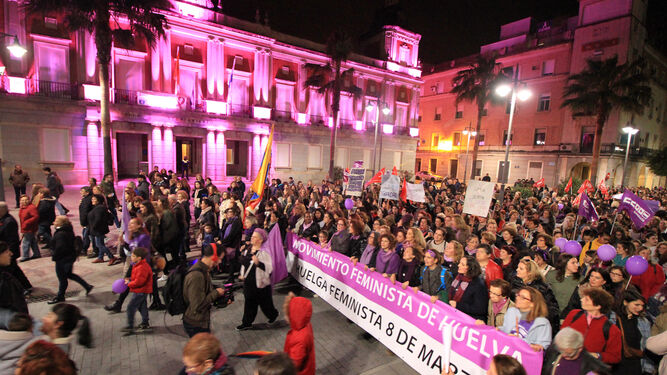 Los manifestantes ante el Ayuntamiento de Huelva, cuya fachada estaba iluminada con el color morado.