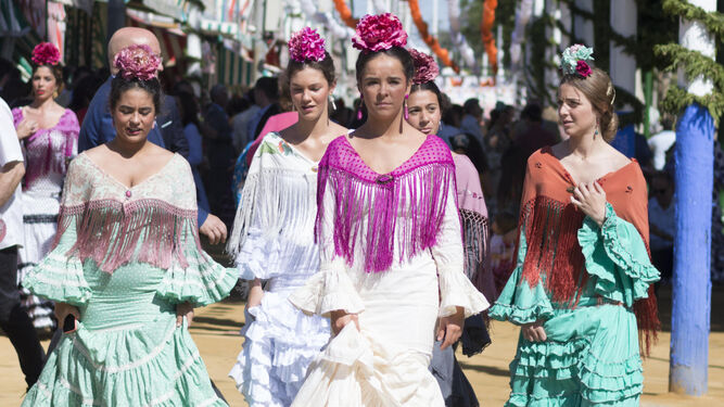 Varias jóvenes pasean por el Real de la Feria de Sevilla vestidas de flamenca.