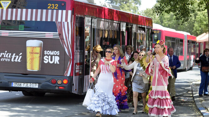 Mujeres vestidas de flamenco se bajan de un autobús de Tussam en la parada de la Feria.