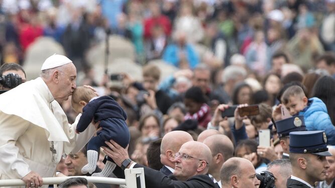 El papa Francisco besa a un bebé a su llegada ayer a la audiencia general en la plaza de San Pedro.