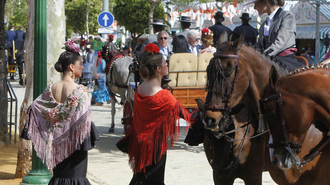 Dos jóvenes vestidas de flamenca conversan con una jinete a caballo.