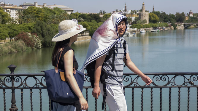 Turistas se protegen del sol  del sol mientras cruzan el puente de Triana.