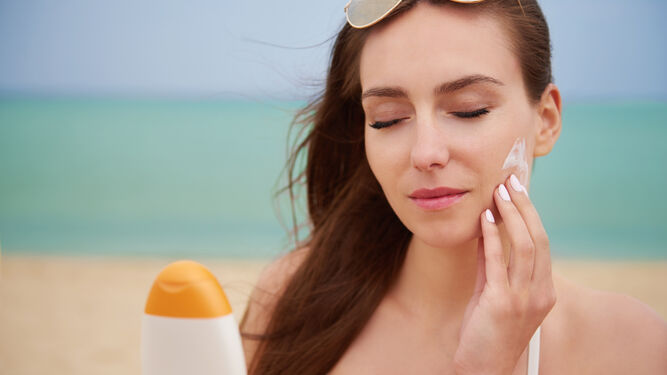 Una mujer se aplica crema solar en el rostro.