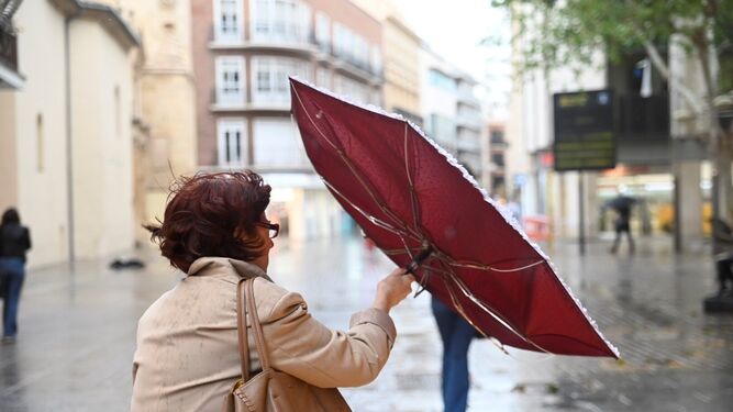 Una mujer sujeta un paraguas volteado por el viento.