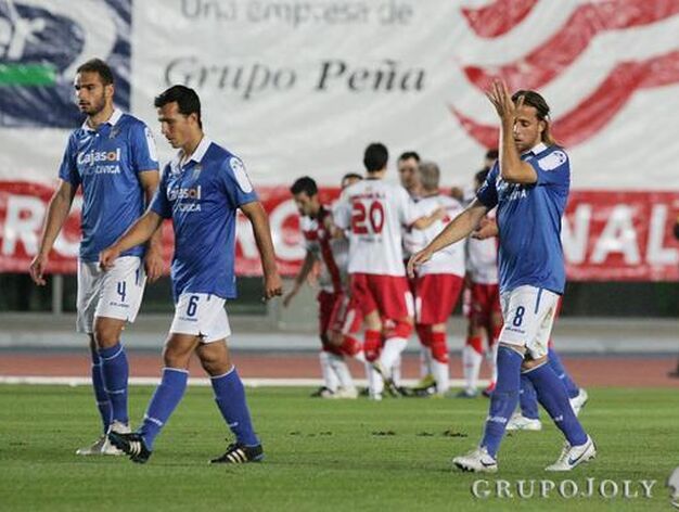 Lomb&aacute;n, Bruno Herrero y Cordero, cabizbajos mientras los jugadores del Huesca celebran el tanto. 

Foto: Pascual