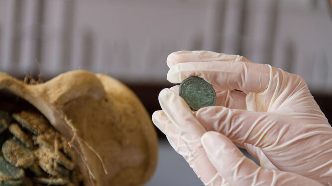 Un investigador muestra una de las monedas halladas en ánforas.