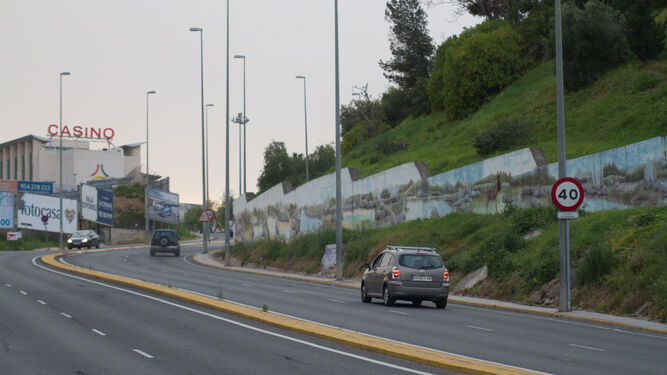 Varios vehículos pasan contra el muro que contiene la ladera afectada por el riesgo de deslizamientos.