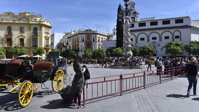 Una turista y coche de caballos junto al vallado de plaza Virgen de los Reyes