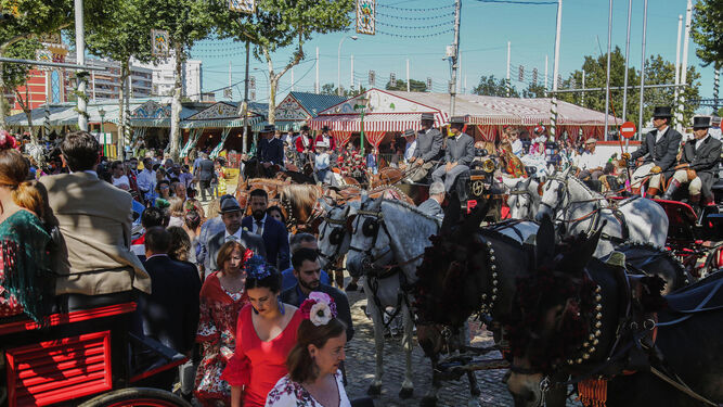 Caballistas, mujeres vestidas de flamenca y coches de caballo en una abarrotada calle del real.