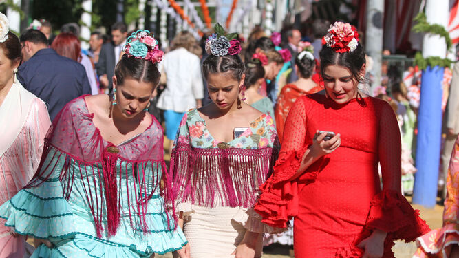 Tres jóvenes vestidas de flamenca atraviesan el real de Los Remedios en la pasada edición de la Feria de Abril.
