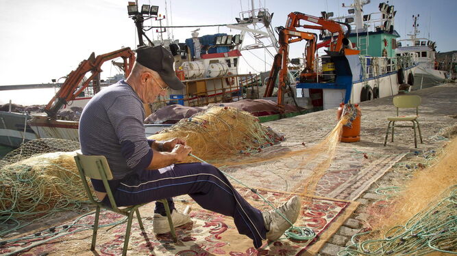 Un pescador de Barbate cose las redes mientras la flota pesquera permanece amarrada al puerto de la localidad.