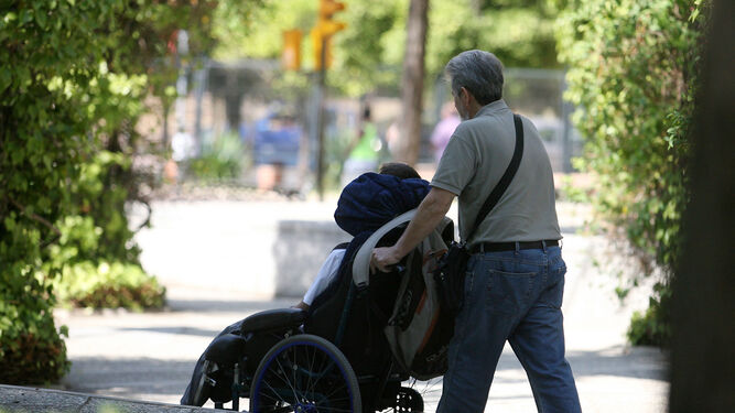 Un hombre empuja la silla de ruedas de una persona en situación de dependencia.