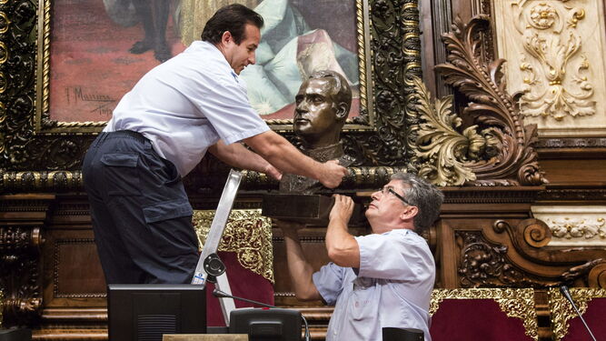 Dos operarios municipales retiran el busto  del Rey Juan Carlos I del salón de plenos del Ayuntamiento de Barcelona.