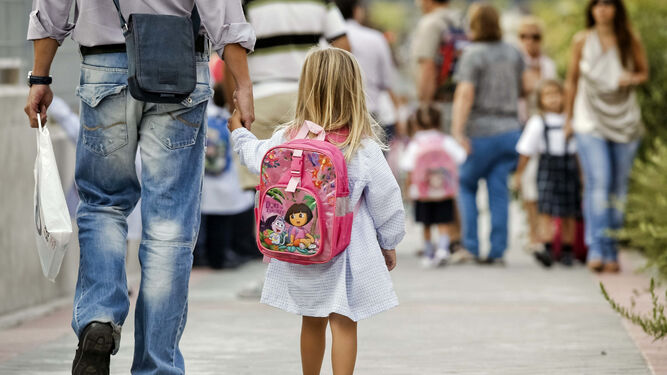 Una niña de la mano de su padre camino de clase al inicio del curso escolar.