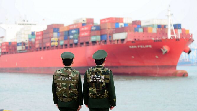 Dos guardias fronterizos ante un barco cargado de contenedores mientras hacen guardia en el puerto chino de Qingdao.