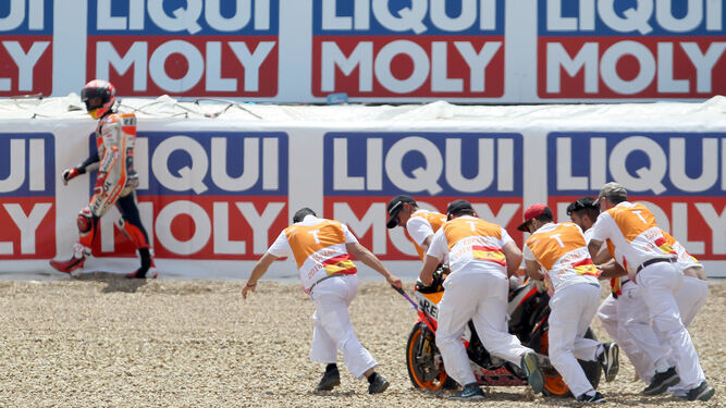 Varios comisarios de pista retiran la Honda 93 de la escapatoria de Dry-Sack mientras Marc Márquez camina cabizbajo.