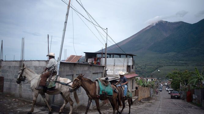 Dos hombres montados a caballo observan la erupción del Volcán de Fuego.