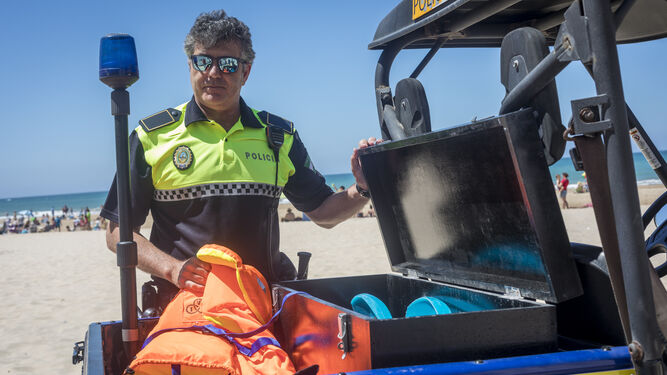 El agente, con un vehículo policial en la playa.