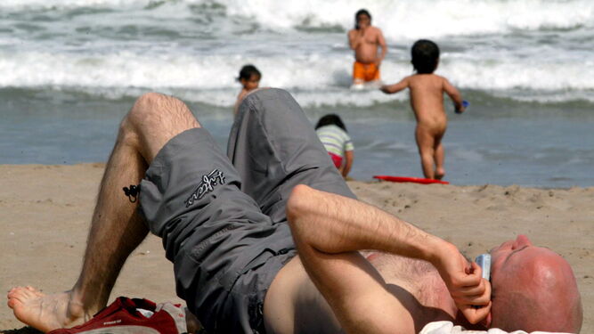 Un hombre habla por el móvil mientras disfruta de la playa.