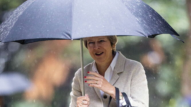 Theresa May, resguardándose de la lluvia bajo un paraguas.