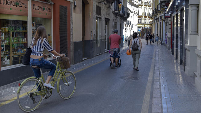 Una joven en bicicleta y varias personas paseando a pie por la calle Amor de Dios.