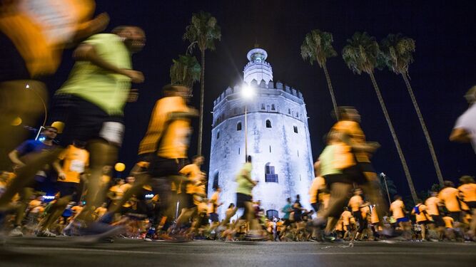 Participantes de la carrera nocturna a su paso por la Torre del Oro