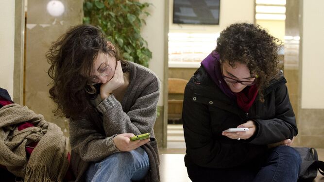 Dos jóvenes estudiantes consultan sus teléfonos móviles en una facultad.