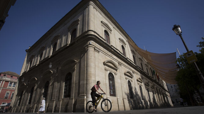 Una joven montada en bicicleta pasa junto a la fachada del Ayuntamiento.