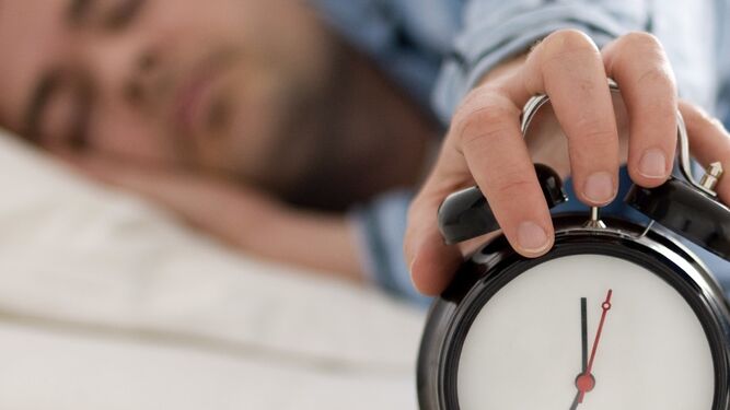 Un joven dormido mientras para la alarma de un reloj.