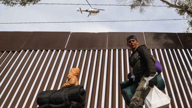 Un helicóptero de la patrulla de EEUU sobrevuela la valla mientras dos inmigrantes caminan rumbo a Tijuana.