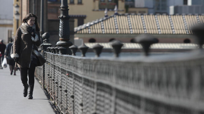 Una joven cruza el puente de Triana abrigada por las bajas temperaturas.