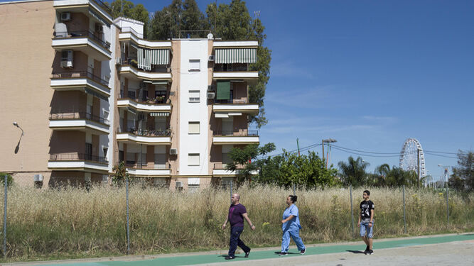 Tres personas caminan junto a las viviendas de la barriada de Tablada.