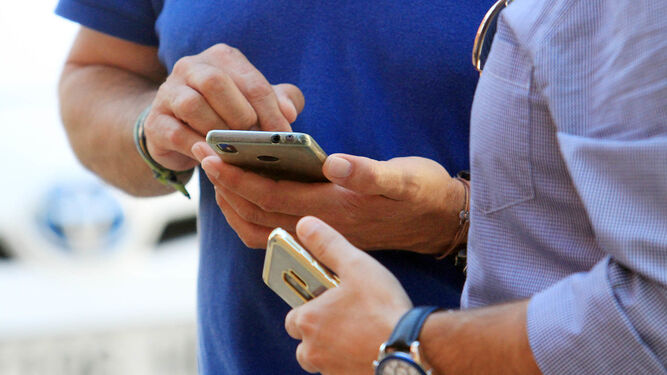 Dos hombres miran sus teléfonos móviles en la calle.