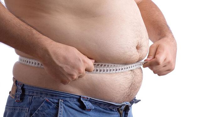 Un hombre mide con un metro el perímetro de su cintura.