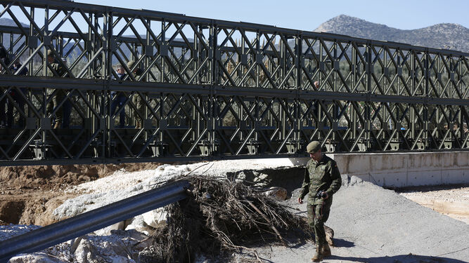 Un militar observa los restos del puente antiguo con el nuevo detrás, en Casariche.