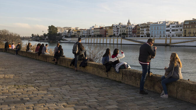Varios jóvenes disfrutan del sol en una de las orillas del río en Sevilla.