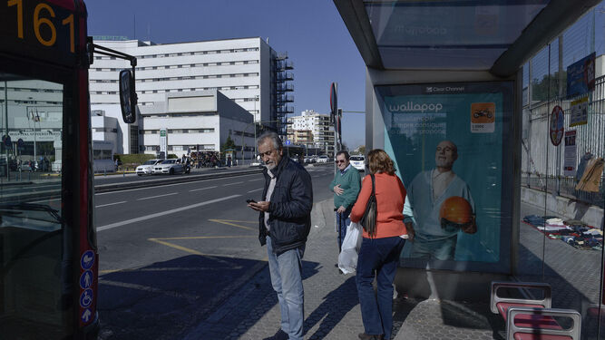 Un hombre mira el móvil en una parada del autobús frente al hospital Virgen Macarena.