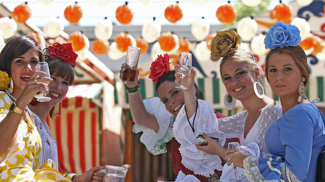 Mujeres vestidas de flamenca en un coche de caballos, bebiendo rebujito.