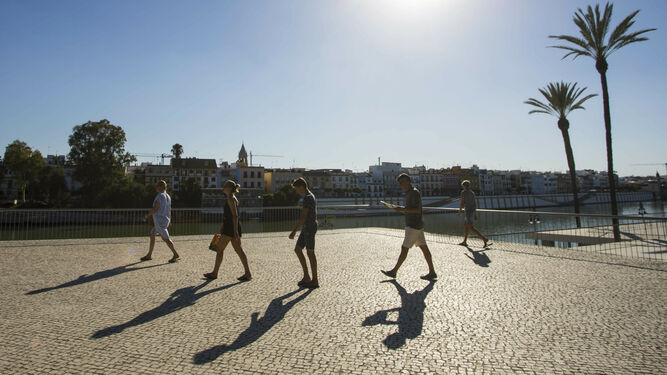 Personas paseando a orillas del Guadalquivir bajo un sol radiante