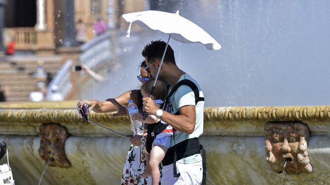 Turistas se fotografían en la Plaza de España cubiertos con una sombrilla.