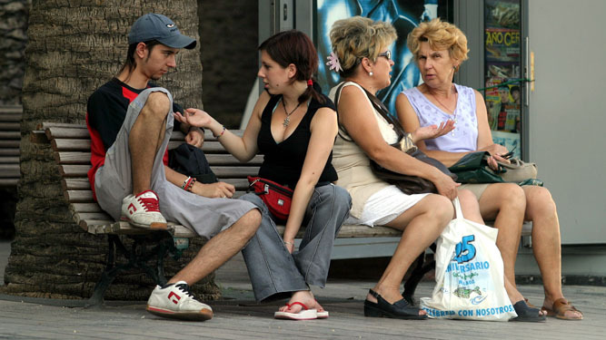 Una pareja de jóvenes comparten un banco  con dos señoras de mayor  edad.