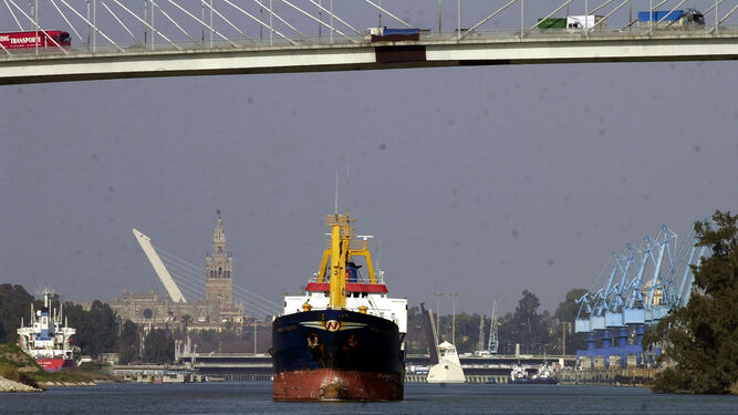 Un buque mercante navega por el Guadalquivir con la Giralda y el puente del Alamillo al fondo.
