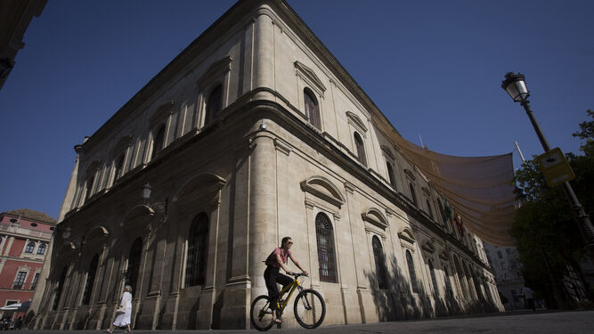 Dos mujeres, una caminando y otra en bicicleta, pasan junto a la fachada de la Casa Consistorial que da a la calle Granada.