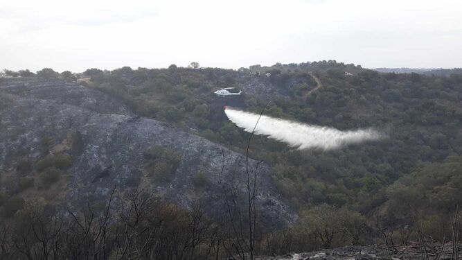 Un helicóptero refresca el terreno en El Ronquillo.